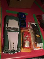 Overview of all four model vehicles: two-tone vintage car, small blue truck, red sports car in plastic case, and boxed green-yellow train model