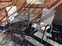 Four patio chairs and one square metal patio table placed outdoors against brick wall.