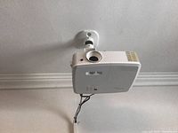 Front and bottom view of ceiling-mounted Optoma projector showing lens, control buttons and LED indicators.