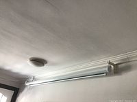 Wall mounted white motorized projector screen in a slim housing near ceiling with visible power cord and wiring, suspended on brackets.