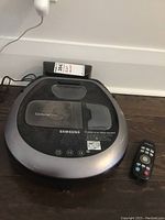 Top view of Samsung CycloneForce robot vacuum on floor with remote control beside it
