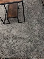 Close up image showing the texture and color of the gray shag rug under a wooden table.