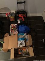 Overall lot showing the power drill, collapsible dolly, ant out spray cans, hand tools in organizer, light bulbs, and tool box in boxes.