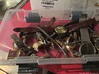 Plastic container with multiple wristwatches piled inside, various bands and faces visible.