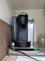 Silver Keurig single-serve coffee maker on a metal stand with a drawer, located on a shelf.