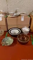 Bowls, platters, and glassware arranged on cardboard boxes, showing the set of Pyrex bowls, two Asian style bowls, and two other glass bowls.