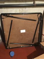 Bottom view showing black folding metal legs attached to the underside of the table surface.