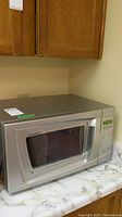 Silver Sylvania microwave on countertop beneath wooden cabinets.
