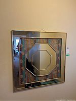 Front view of square wall mirror showing octagonal mirror inset with geometric floral background and metal frame