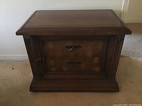 Front view of closed wooden two drawer night table showing dark wood finish and carved side details.