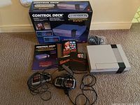 NES console, original Control Deck box, two controllers, Super Mario Bros box and manuals, cables arranged on carpet