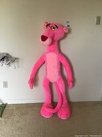 Front view of large Pink Panther stuffed toy standing against a white wall showing full body, facial details, and color.