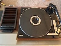 Top view of Sanyo turntable with belt drive and one speaker unit showing wood base and black platter with tonearm and control panel details.