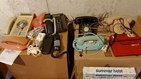 Eight assorted corded telephones displayed on two cardboard boxes