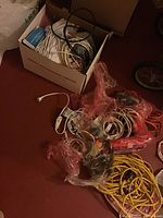 Overview of two boxes with various wires, cables, extension cords, and some other small items scattered on the floor.