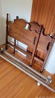 Wooden headboard and footboard leaning against wall near metal bed frame rails on floor.
