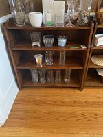 Front view of the wooden bookshelf showing three shelves with glassware placed on them, highlighting size and wear.