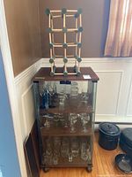 Full view of the glass-fronted cabinet with glassware inside and wooden wine rack on top