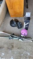 Shows two pairs of children's skis (one pair Rossignol Fun 2), three helmets (one pink ski, one black ski, one black hockey), boxed KeBo hanging light fixture, and shower set parts.
