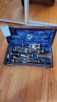 Clarinet disassembled inside open blue velvet-lined case, showing all 5 main sections and a lyre music holder