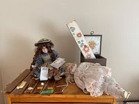 Two dolls, a small teddy bear, golf-themed wooden wall hangings, and a painted board arranged on top of a wooden chest