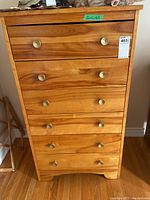 Front view of wooden highboy dresser with six drawers and round metal knobs, showing wood grain.