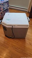 Front and side view of the Igloo electric cooler showing power cord and venting system on side panel.