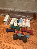 VHS tapes, fitness DVDs, and various colored hand weights of different sizes laid out on floor.