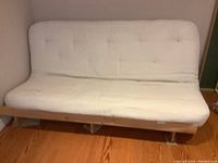 Full view of futon with pine wood frame and white tufted mattress, showing seat and backrest area.
