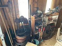 Image of various gardening tools including brooms, rakes, forks, and tomato cages stacked beside pots.
