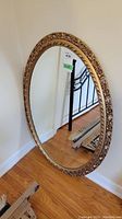 Full view of the large oval mirror leaning against the wall, showing the entire mirror and frame shape.