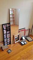 Photo showing large rectangular mirror standing on floor with assortment of picture frames in front, including a black collage frame with multiple images and inspirational quotes.