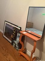Framed posters of National Geographic Grand Canyon and Fundy Park leaning against wall next to modern demi lune wooden table with curved legs.