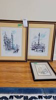 Three framed prints on floor: two larger prints with architecture and monument, one smaller black and white print with historic building and carriage