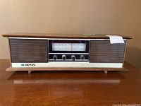 Full front view of Ross solid state AM/FM table radio showing wood grain finish, tuning box, and three control knobs.