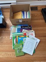 Box of vintage sheet music including various booklets and loose sheets seen on wooden floor.