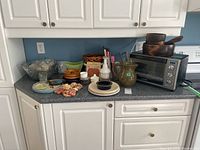 Overview photo showing Black & Decker toaster oven, pitcher, wooden bowls, trays, plates, cookbooks, basket, and assorted kitchenware on countertop