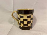 Front side of checkered mug showing handle and pattern with chips and wear.