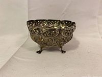 Front side view showing floral and leaf repousse patterns on silver bowl with claw feet.