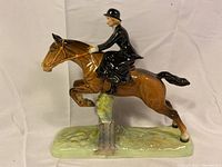 Side view of entire figure showing huntswoman on horse jumping fence