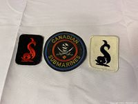 Three military badges: one circular 'Canadian Submarines' patch and two rectangular patches with red stylized emblems on black and white backgrounds.