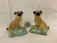 Front view of the pair of antique porcelain pug dog figures seated on blue floral cushions.