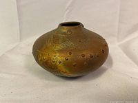 Side view of the rounded copper-colored pottery vase, showing textured surface and raised dotted decoration around the upper part.