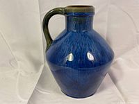 Front view of the electric blue pitcher vase with greenish-brown handle and rim, showing bulbous body shape and shiny glaze.