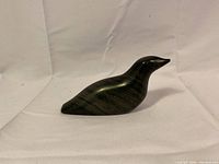 Side view of the vintage Inuit soapstone bird carving showing sleek, polished dark stone with natural striations and a stylized shape.