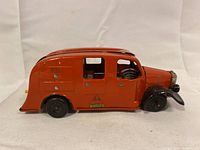 Full side profile of the orange tinplate toy car showing overall condition and paint wear.