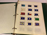 Photo of a binder page with vintage US state flag stamps including Kansas, Tennessee, Texas, Utah and others, arranged neatly on lined paper with handwritten state names.