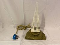 Front view of the lamp showing clear triangular body, internal etched clock tower, and square brown base with electrical cord.