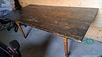 Side view of rectangular wooden kitchen table showing weathered dark finish top and turned wood legs.
