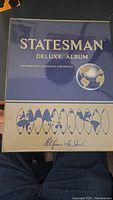 Photo of the closed blue hardcover Statesman Deluxe Album for postage stamps of the world, showing brand and album series.